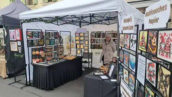 Stand Laz’Arts Factory au Marché de Noël de Carouge 2025, présentant des créations artisanales en découpe et gravure laser ainsi que des œuvres multicouches en papier, exposées sous une tente blanche sur un marché extérieur.